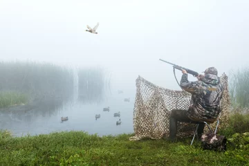  A hunter with a hunting gun and hunting form to hunt in an autumn season on ducks. Hunting period. The man is on the hunt. Hunter man. © Sergey