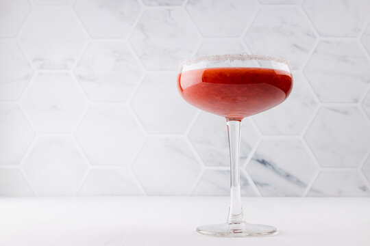 Summer fresh fruit strawberry cocktail of grinded red berry with sugar rim in glass goblen on white wood table with marble tile wall.