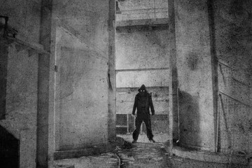 A demonic hooded figure with glowing eyes, standing in an abandoned industrial building. With a grunge, textured edit.