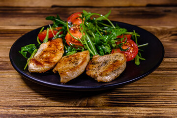 Roasted chicken breasts and salad with arugula and cherry tomatoes in a black plate