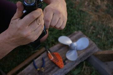 Human hands repairing a propeller boat engine. In the background is the engine propeller and repair tools.