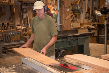 Furniture maker feeding a board through a tablesaw in woodshop - obrazy, fototapety, plakaty