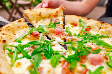 woman Hand takes a slice of meat neapolitan Pizza with Mozzarella cheese, ham, bacon, Spices and chicken in cafe outdoor