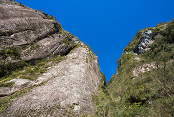 Looking up a natural wall of rock and blue sky.