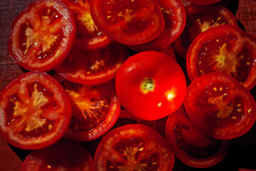 Tomatoes cut into rings on a red background. Lots of tomatoes on a pile on a wooden board. Contrasting light as an artistic effect.