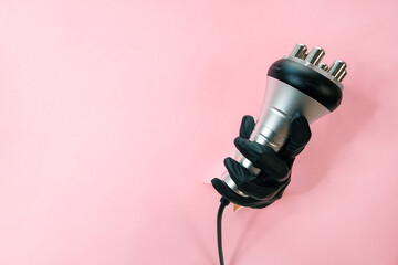 RF lifting hardware massage on a pink background. hand in a black glove with an apparatus.