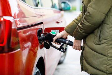 Close-up of hands of woman at self-service gas station, hold fuel nozzle and refuel the car with...