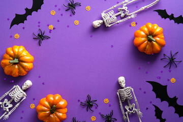 Happy Halloween holiday party composition with pumpkins, skeletons, spiders, bats, confetti on purple background. Top view, flat lay.