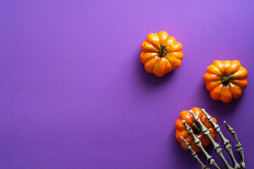 Happy Halloween holiday composition with pumpkins and skeleton hand on violet background. Flat lay,...