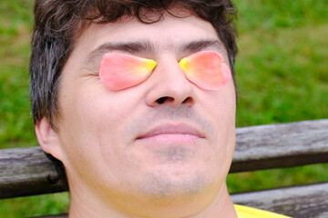 The use of rose oil and rose water, rose petals on the eyelids of a man. Rose essential oil. Selective focus.