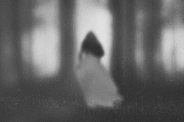 A ghostly transparent woman in a dress standing in a forest. With a blurred, vintage textured edit.