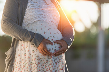 Pregnant woman caressing her belly and making a heart shaped gesture with her fingers signifying...
