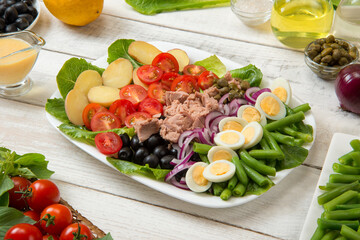Traditional Nicoise salad in a white rectangular salad bowl on an old white table with sauce and...