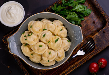 Russian pelmeni meat Dumplings with greens in a black plate. Russian traditional cuisine. Top view. Free copy space.