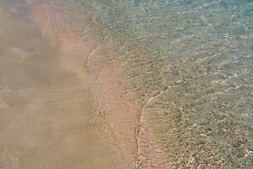 Fototapeta na wymiar Clear waves and colorful sand on tropical sandy beach in Crete Greece.