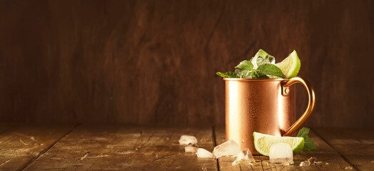 Moscow mule cocktails in copper mug with lime, ice, ginger beer, vodka and mint. Wooden background, bar tools, negative space