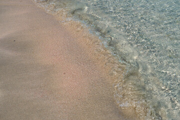 Clear waves and colorful sand on tropical sandy beach in Crete Greece.