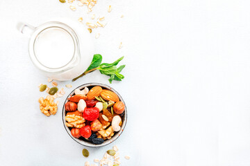 Muesli bowl and ingredients for healthy breakfast. Granola, nuts, dried fruits, flakes and greek yogurt on white table copy space