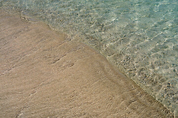 Clear waves and colorful sand on tropical sandy beach in Crete Greece.