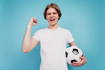 Photo of positive crazy man holding soccer ball raise fist isolated blue background