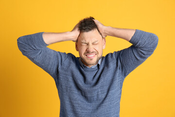 Man suffering from terrible migraine on yellow background