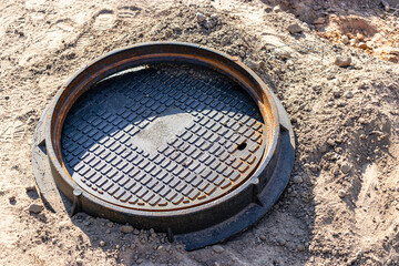 A cast-iron sewer manhole prepared for installation. Close-up. Road works. Shelter for underground utilities.