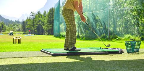 Golf player wearing plaid pants practices his golf swing on driving range, view from behind 