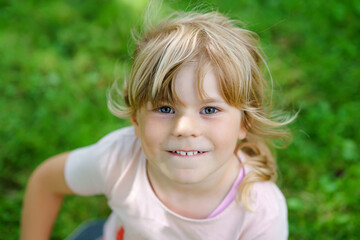 Portrait of happy smiling preschool girl outdoors. Little child with blond hairs looking and smiling at the camera. Happy healthy child enjoy outdoor activity and playing.