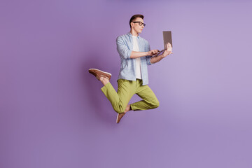 Portrait of freelancer athlete guy jump hold netbook look screen on violet background