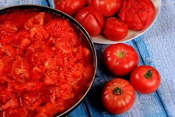 Closeup of boiling chopped red tomatoes sauce in a pan on the stove, blue wooden board background. Blanched tomatoes 