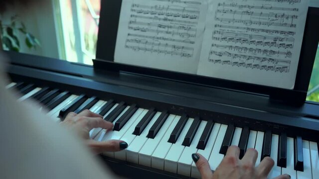 The Woman Pianist Looks At The Notes And Plays The Piano. The View From Behind The Pianist.