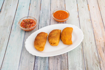 serving of Colombian corn empanadas stuffed with shredded chicken meat are sauces and aji to dip