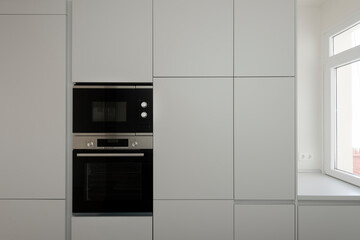 Fototapeta premium front wall of gray kitchen furniture with microwave oven and window