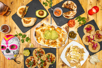 Obraz na płótnie Canvas Top view image of set of Mexican dishes and catrina mask. Cochinita pibil tacos, pastor tacos, nachos with guacamole, quesadillas, jalapeños, limes and cilantro