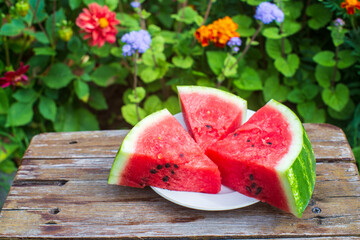 Slices of fresh red watermelon on a plate on a wooden surface in the garden against a background of...