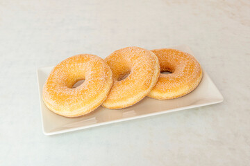 Tray with three sugar donuts with holes on a white tray