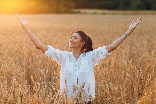 Happy young woman on wheat field with raised up hands enjoying freedom, autumn harvest concept.