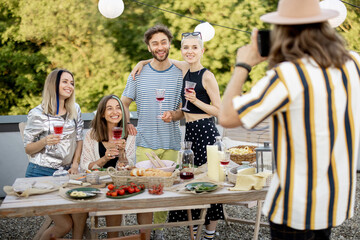 Young stylish people hang out at picnic outdoors, having fun making a group photo at dining table on a roof terrace