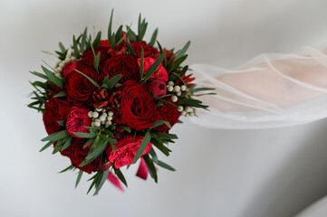 The bride holds a beautiful bouquet of red roses and peonies at arm's length.