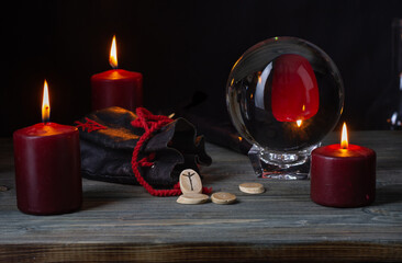 The Algiz rune. A composition of red burning candles, an old leather bag for Scandinavian runes and a crystal ball on an old wooden table.Algiz is a rune of protection and life.