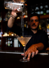mixologist pouring the martini into the glass
