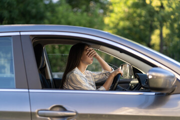 Stressed girl with headache driving car touching forehead with hand. Frustrated young female driver...