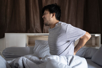 Young Asian man with back pain on the bed at home in the morning after wake up