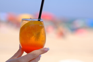 Female hand holding glass of orange alcoholic cocktail on the beach