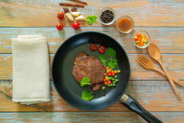 Grilled beef steak and roasted vegetables on dark wooden table background, top view. Juicy meat dish with sauce, rosemary, peppers and cutlery in fry pan. Restaurant food