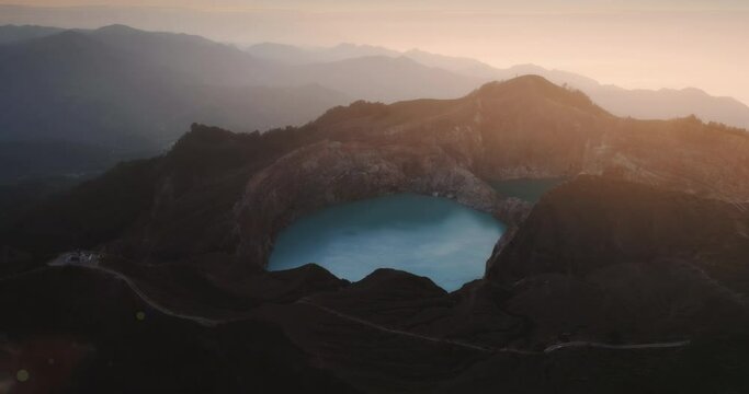 Sunset over blue water in Kelimutu lake volcanic mount, aerial brown rocky mountains surround. Orange pink sky over crater on Flores Island in Eden, Indonesia. Exotic travel tour in Asia. Drone, view.