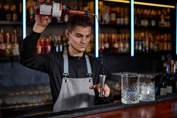 Bartender in apron adds ingredient to glass