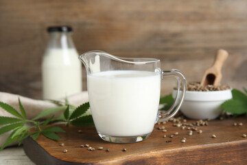 Glass jug with fresh hemp milk, seeds and leaves on wooden board