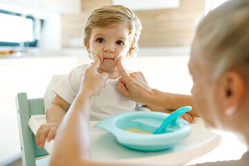 Mom feeds the baby. Young woman feeds her baby from a spoon at home. High quality photo.
