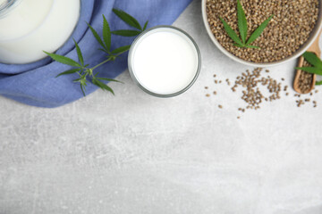 Obraz na płótnie Canvas Hemp milk and seeds with fresh leaves on light grey table, flat lay. Space for text